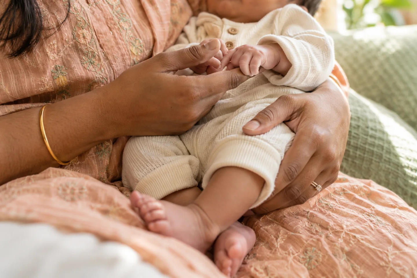 Illustrative image of a parent cradling a clothed newborn, with the baby holding a finger